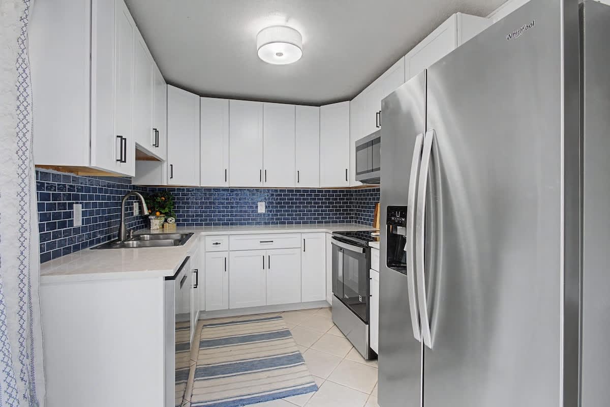 Your sleek, fully-equipped kitchen features pristine white cabinets, stylish blue subway tile backsplash, and premium stainless steel appliances for culinary adventures.