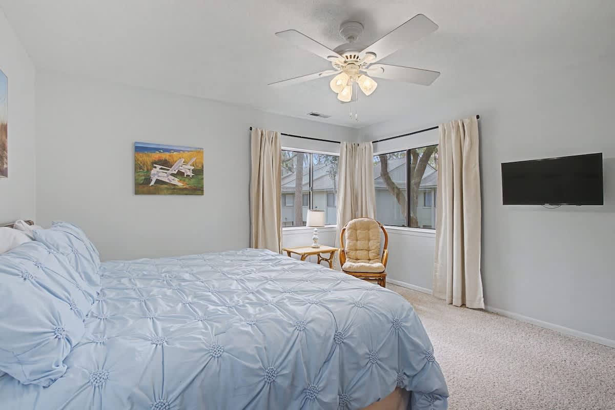 Relax in your peaceful bedroom with soft blue linens, cozy seating by the window, and entertainment at your fingertips.