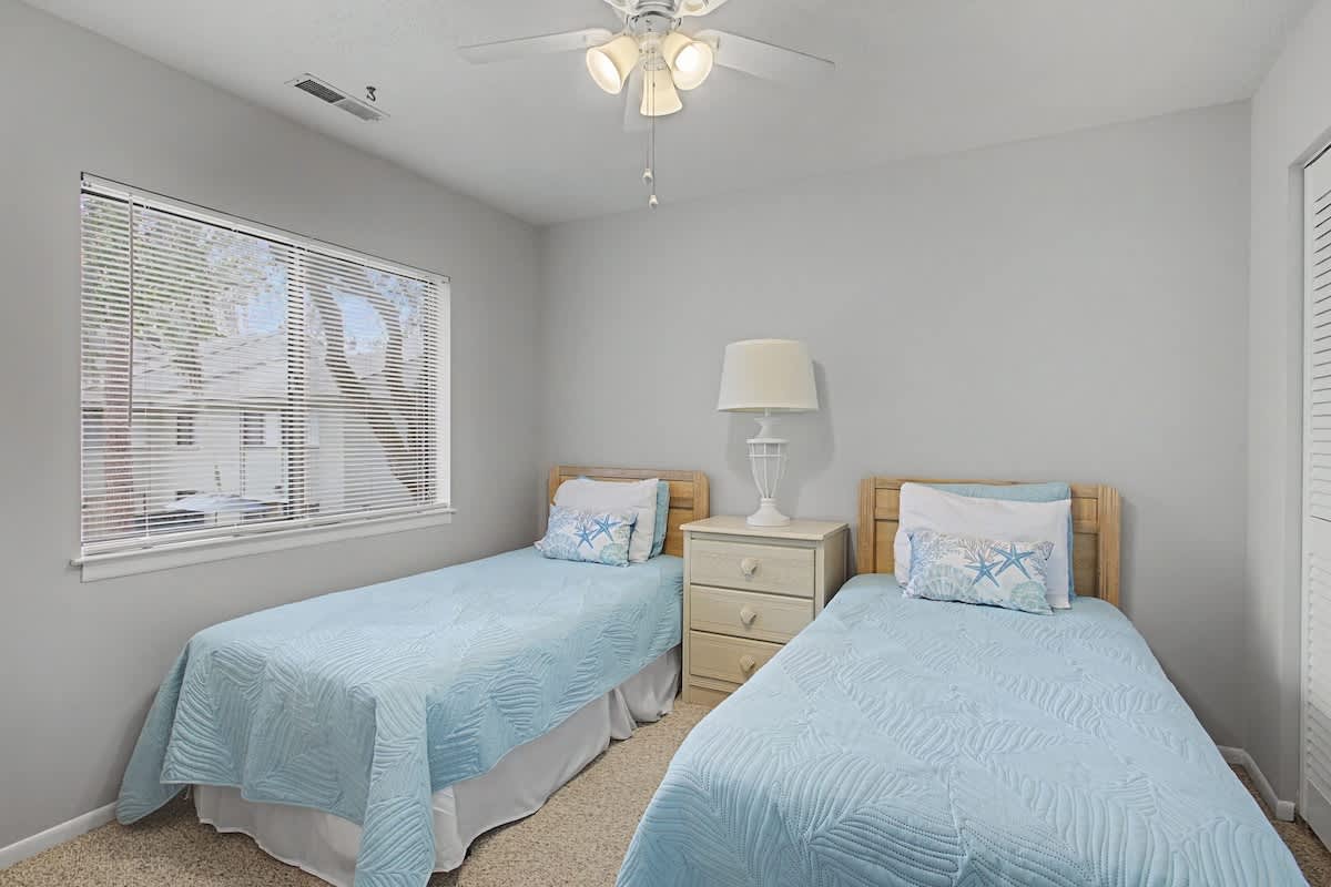 Rest peacefully in your bright twin bedroom with soft blue linens and gentle natural light streaming through the window.