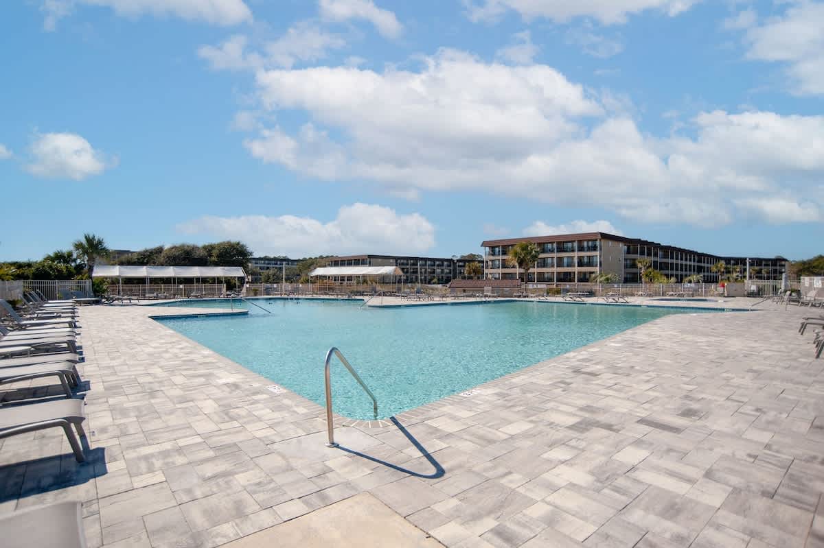 Large resort-style swimming pool with expansive deck and multi-story buildings in a tropical coastal setting.
