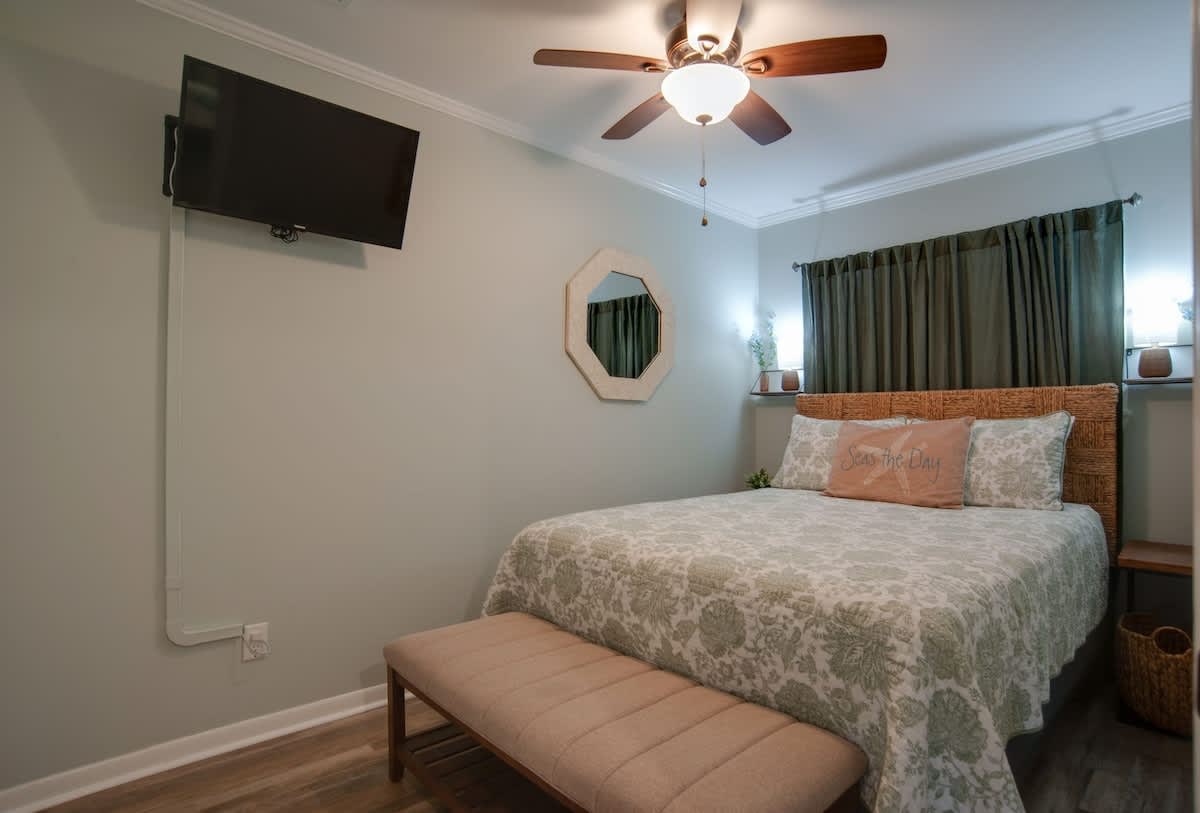 Drift off in your serene bedroom featuring a plush bed, calming decor, wall-mounted TV, and gentle ceiling fan for perfect comfort.