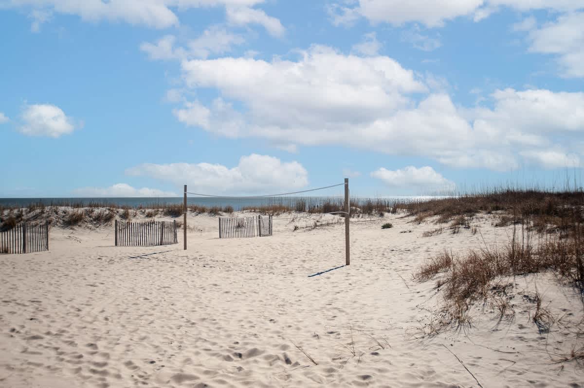 Protected sandy beach area with dune fencing and natural vegetation under partly cloudy skies.