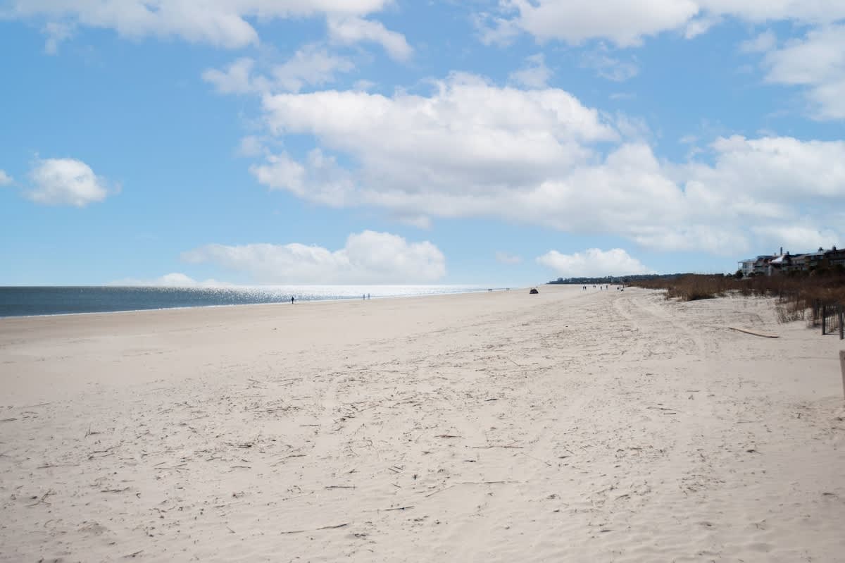 Expansive sandy beach stretches along the coastline with gentle waves and scattered beachgoers enjoying the pristine waterfront setting.