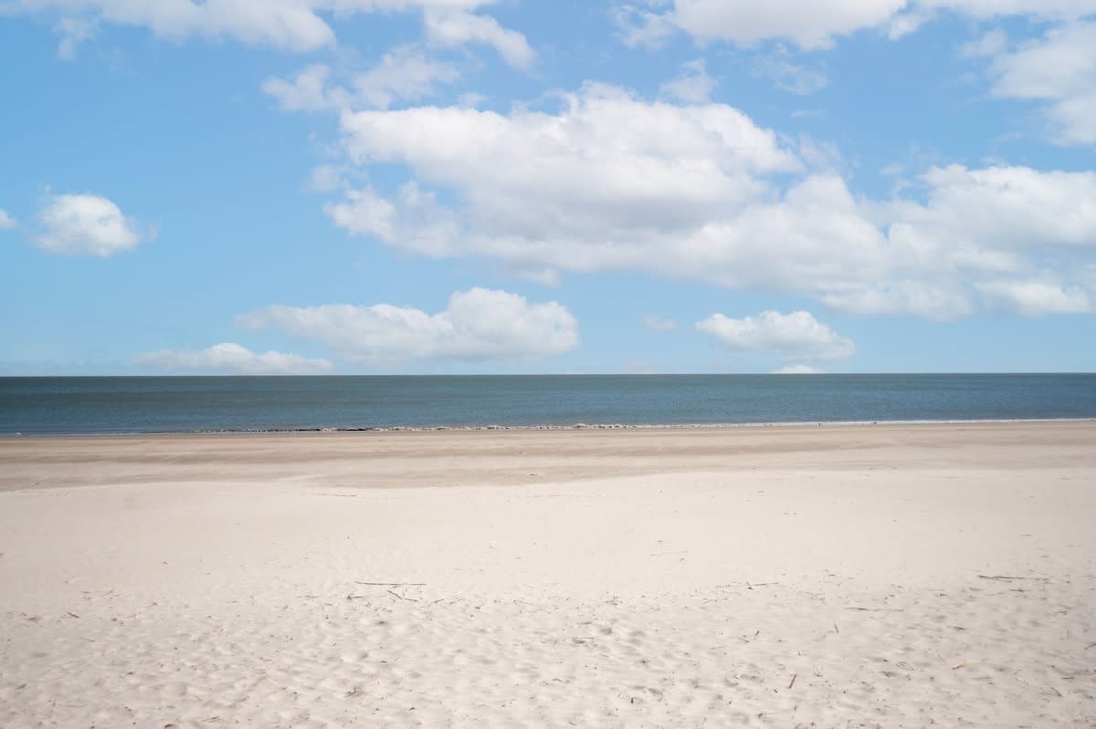 Pristine sandy beach stretches endlessly under dramatic cloudy skies, with calm ocean waters creating the perfect coastal backdrop.