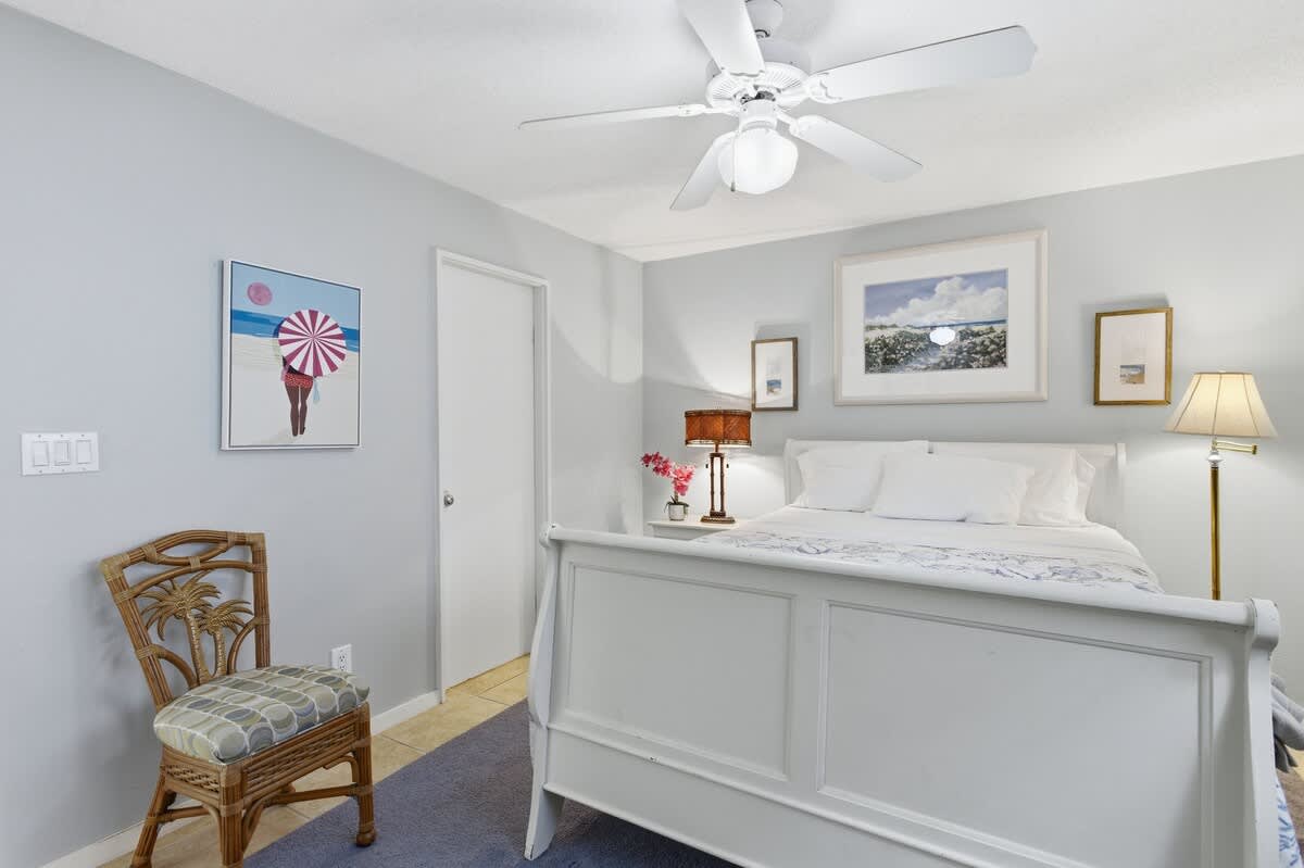Rest peacefully in your serene bedroom featuring a comfortable queen bed, coastal artwork, and gentle ceiling fan breeze.