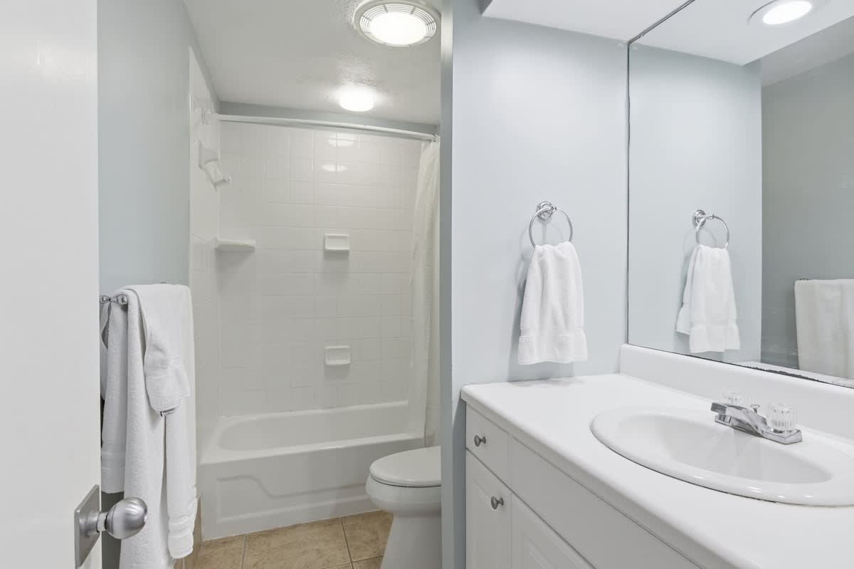 Fresh white bathroom with tub-shower combo and plush towels waiting for your relaxing soak.
