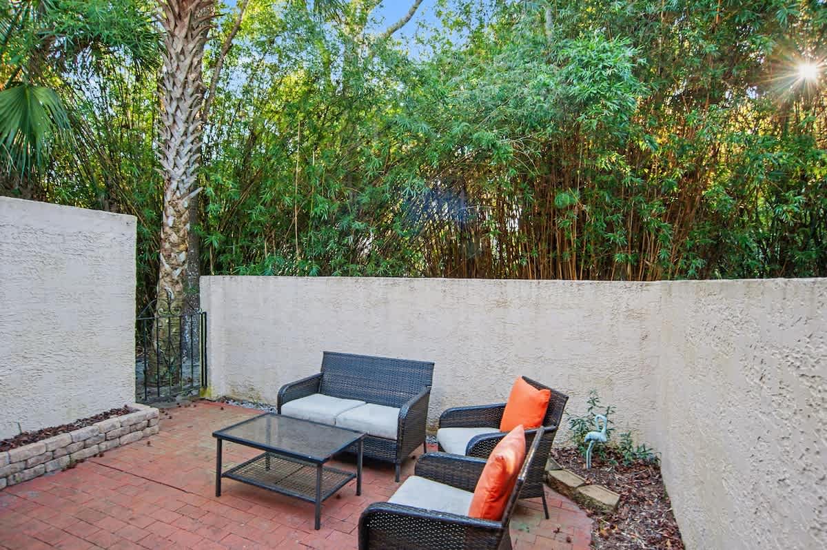 Unwind in your private patio oasis, where wicker furniture and vibrant cushions create the perfect outdoor retreat beneath tropical foliage.