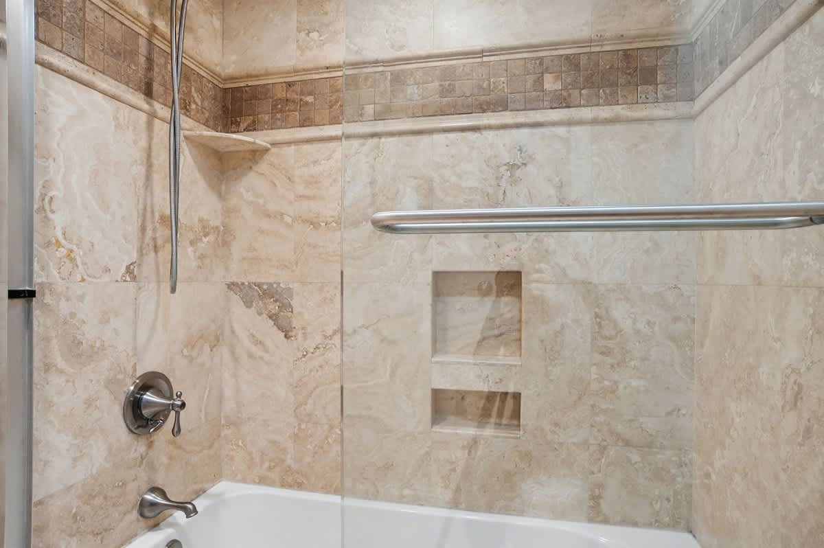 Indulge in your private marble-lined bathroom featuring elegant travertine tiles, built-in storage niches, and a luxurious soaking tub.