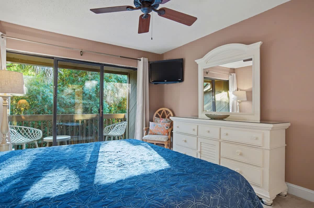 Relax in your peaceful bedroom with garden views through sliding doors, complete with ceiling fan and cozy seating nook.