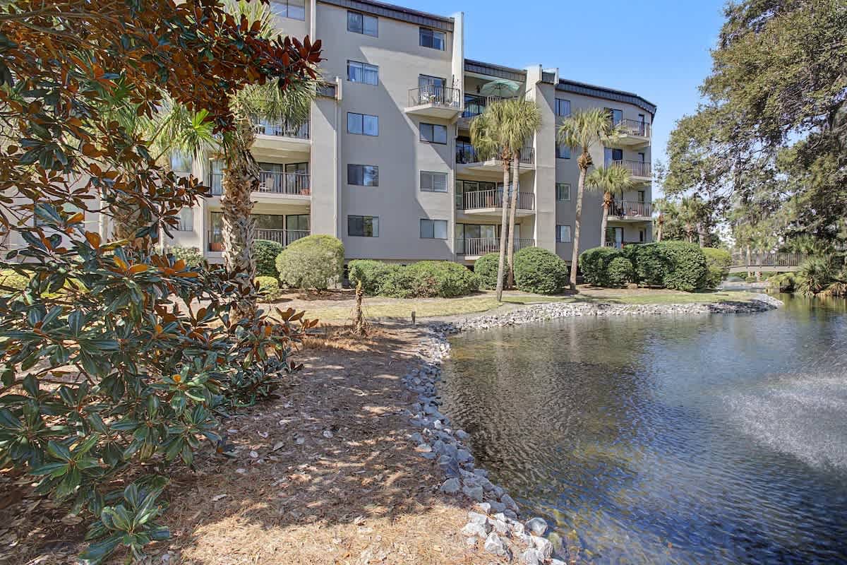 Multi-story waterfront property featuring private balconies and tropical landscaping along a peaceful water feature.