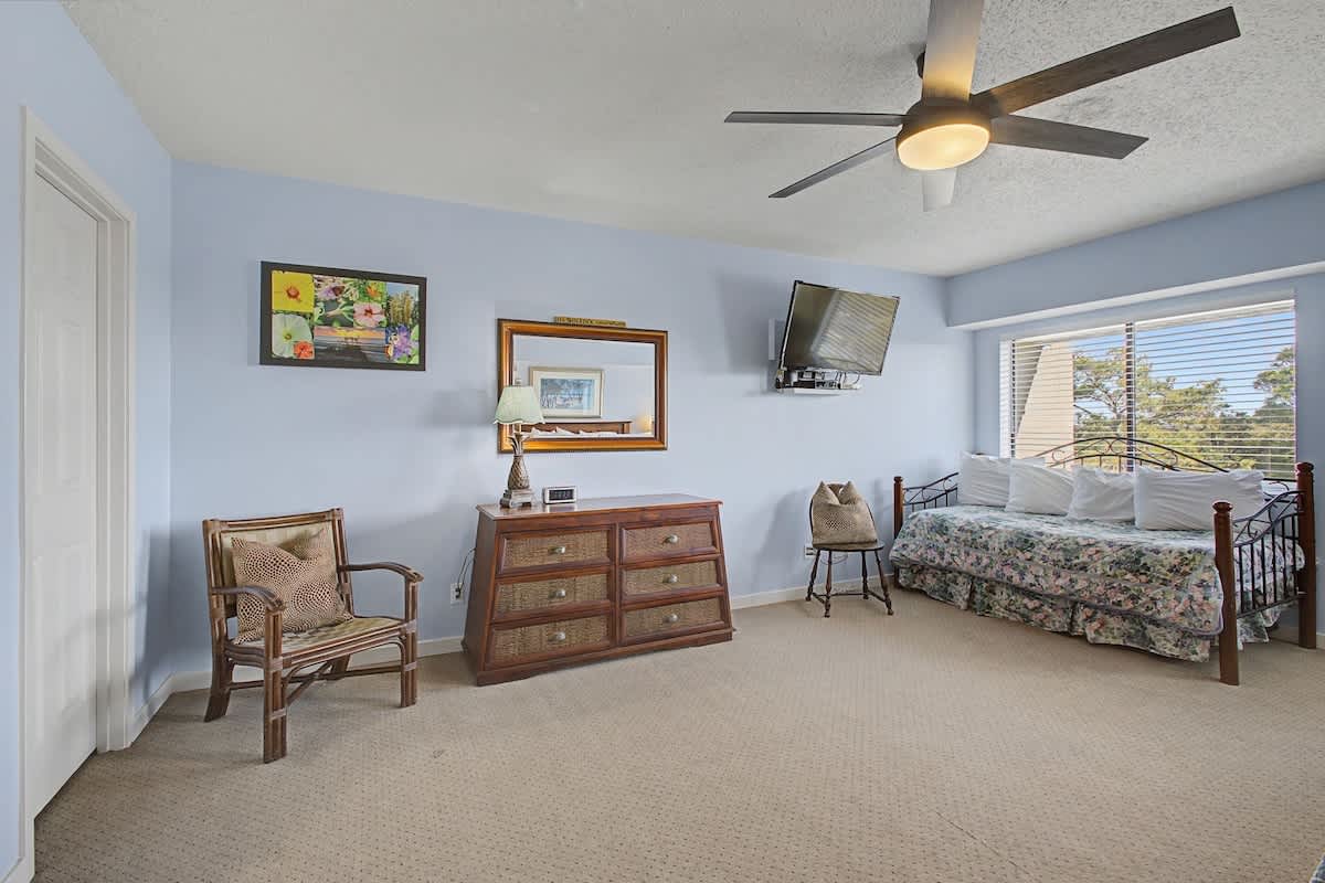 Relax in your spacious bedroom with coastal charm, featuring a ceiling fan for comfort and natural light streaming through the windows.