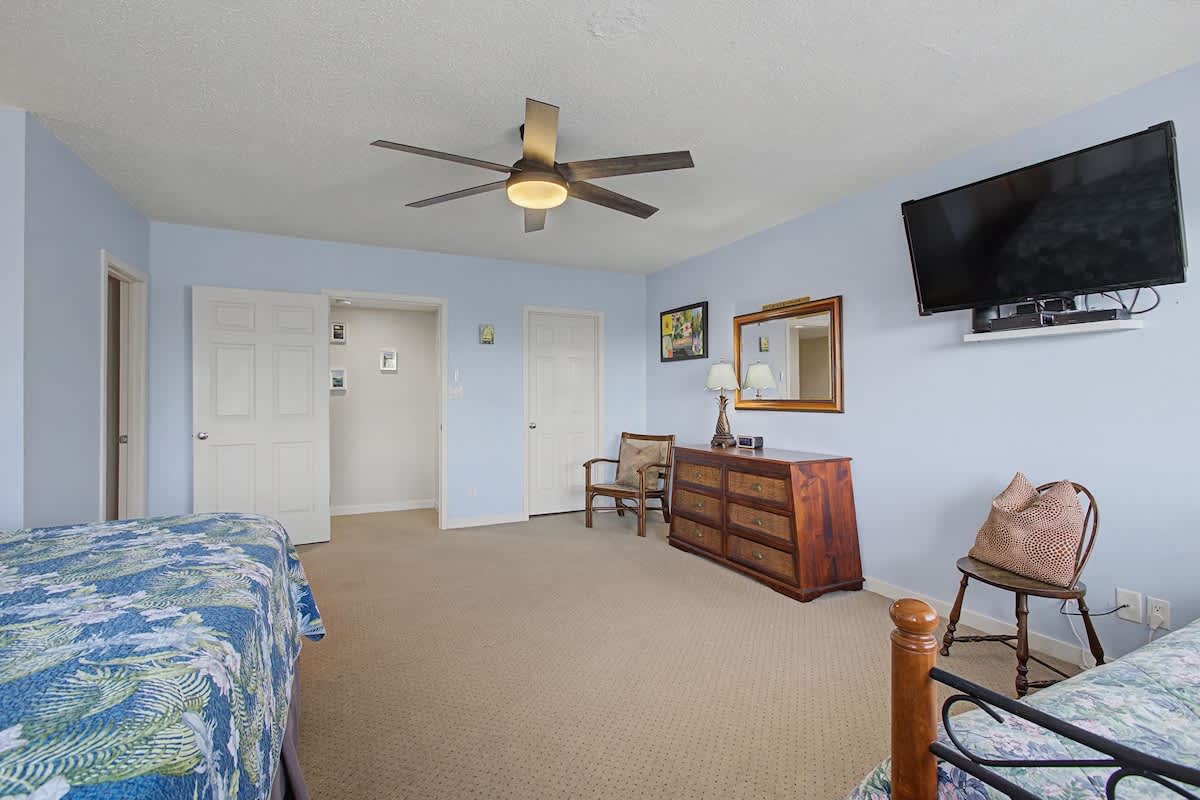 Your spacious bedroom features comfortable beds, warm blue walls, a ceiling fan, flat-screen TV, and classic wooden furnishings for a peaceful stay.