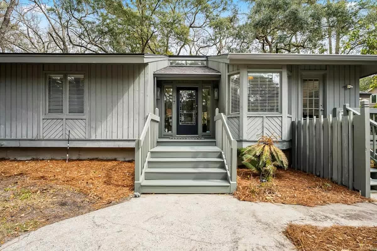 A charming coastal retreat with natural wood siding and welcoming front entrance, nestled among mature trees for privacy and tranquility.