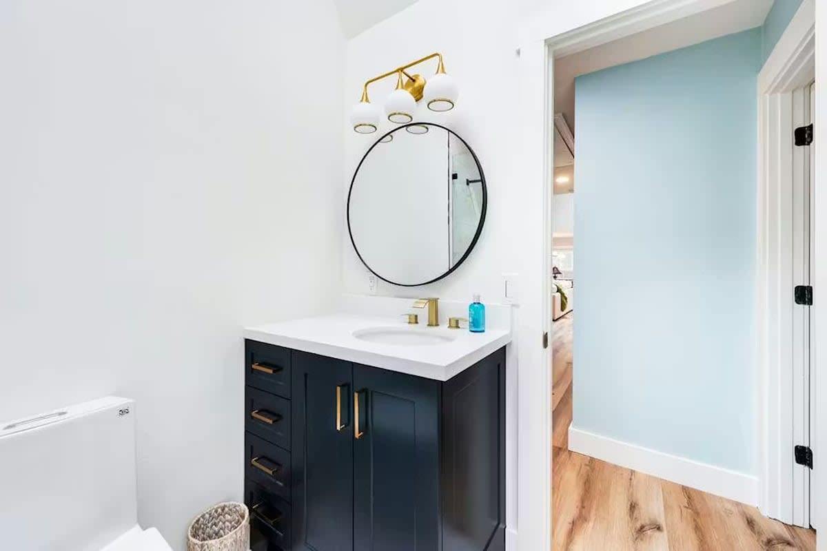 Step into this elegant bathroom featuring a striking navy vanity with brass fixtures and a sophisticated round mirror.