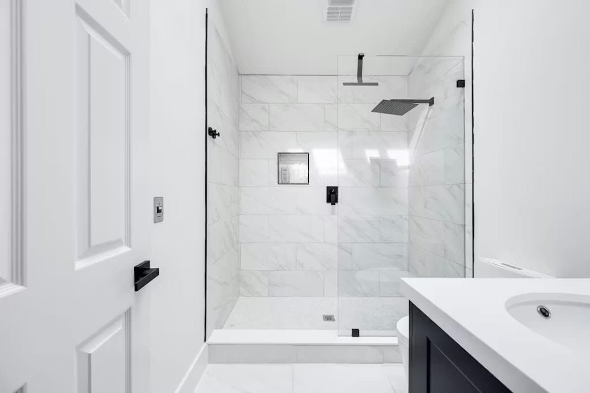 Step into your spa-like sanctuary with gleaming marble tiles, a spacious glass-enclosed shower featuring dual rainfall heads, and pristine white finishes throughout.