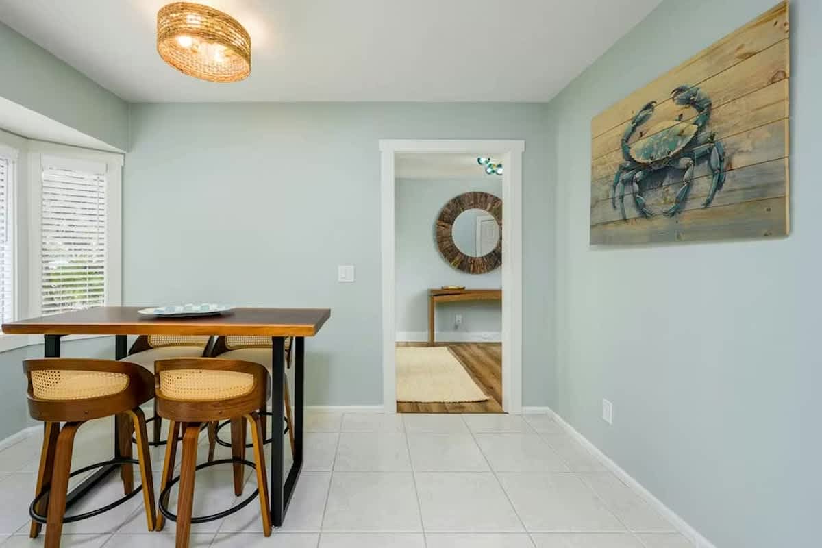 Gather around your stylish dining table beneath warm wicker lighting, where coastal charm meets modern comfort in this inviting space.