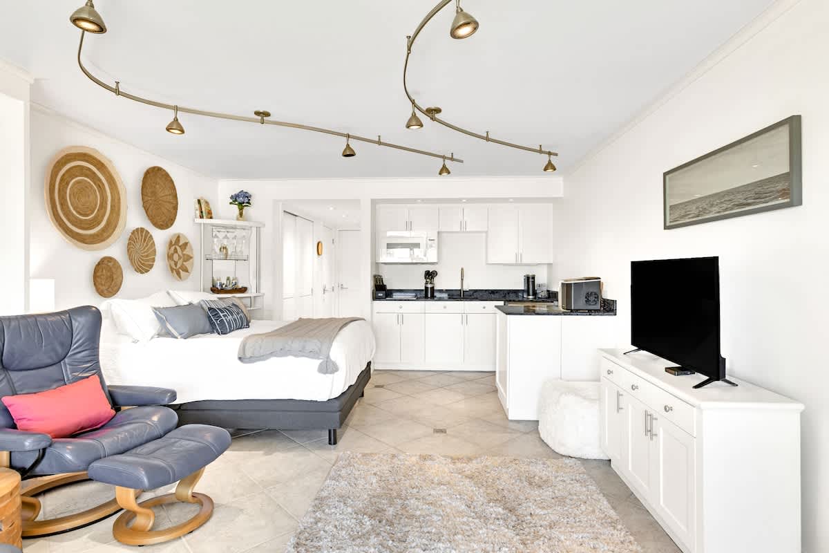 Relax in your bright studio with modern kitchen, cozy seating, and thoughtful touches like woven wall art creating a warm, welcoming atmosphere.