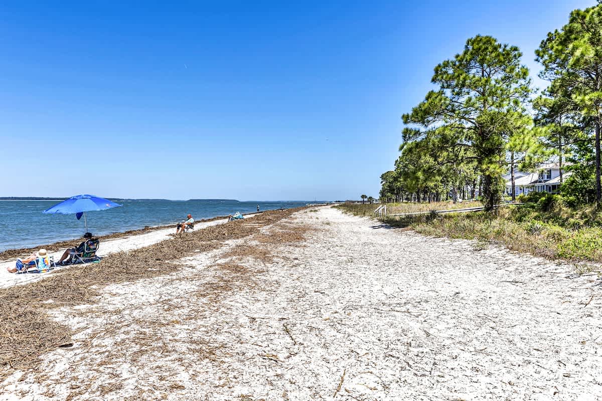 Pristine beachfront stretches along crystal waters, framed by lush coastal trees and charming waterfront homes in this peaceful seaside setting.