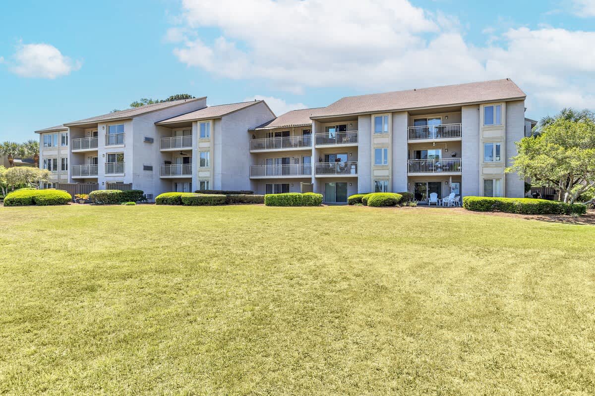 Multi-story vacation rental complex with private balconies overlooking expansive green lawn areas under bright blue skies.