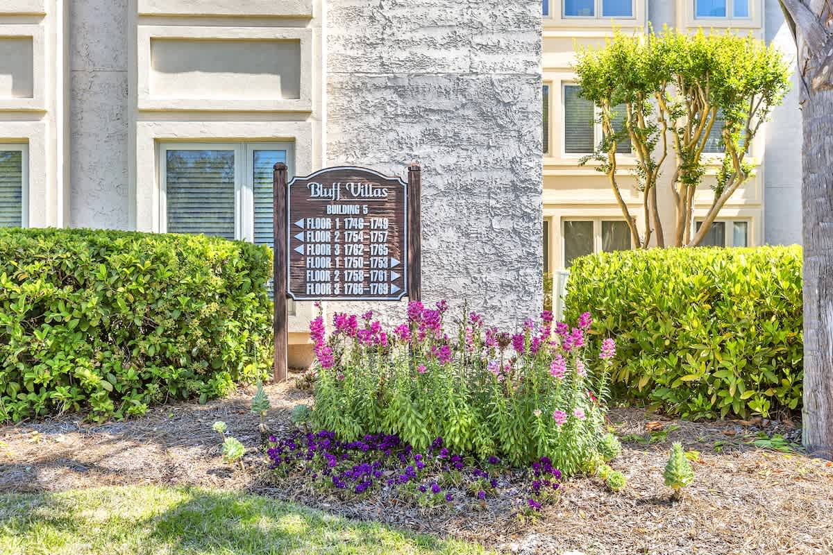Bluff Villas Building 6 entrance marker surrounded by colorful landscaping and mature trees in a well-maintained residential setting.