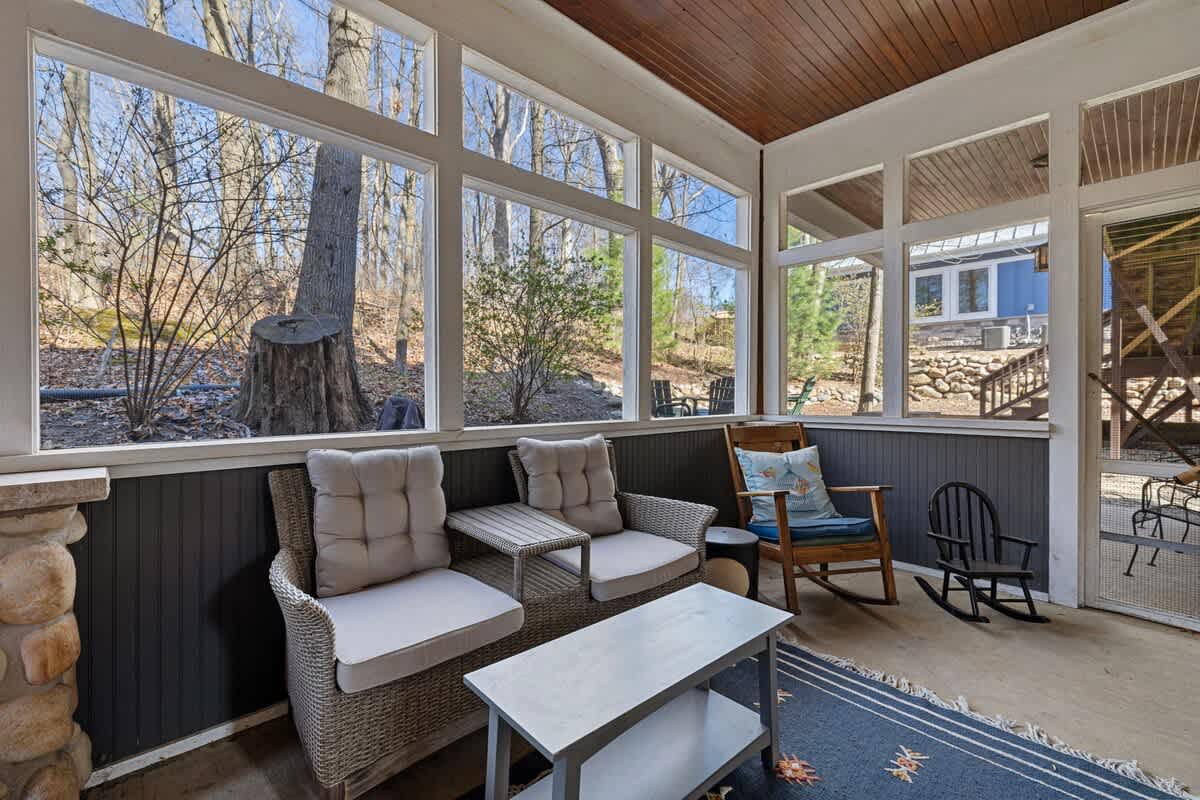 This enclosed patio has a woodsy view, rattan love seat and two rocking chairs!