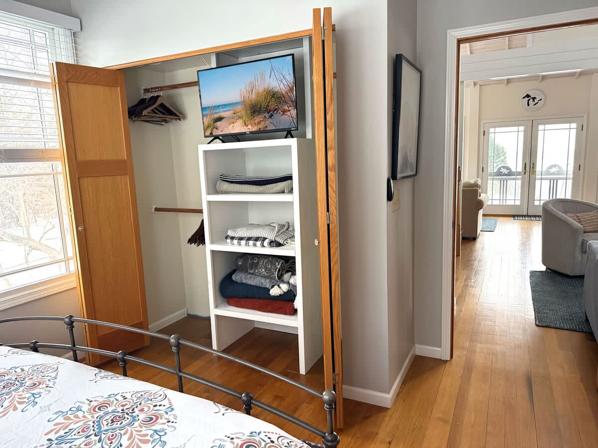 Bedroom 1 closet with built-in shelving, hangers, and a TV for added convenience.