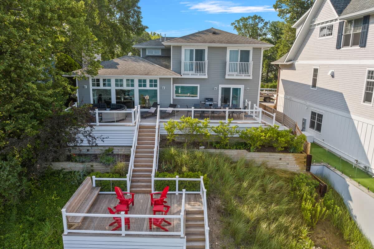 A stunning waterfront property featuring multi-level decks and modern coastal architecture surrounded by lush natural landscaping.