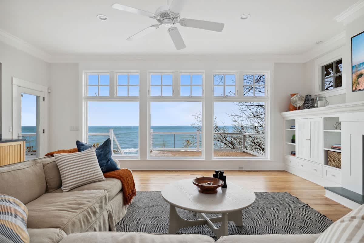 Sink into plush coastal comfort while ocean waves dance beyond your panoramic windows in this bright, airy living space.
