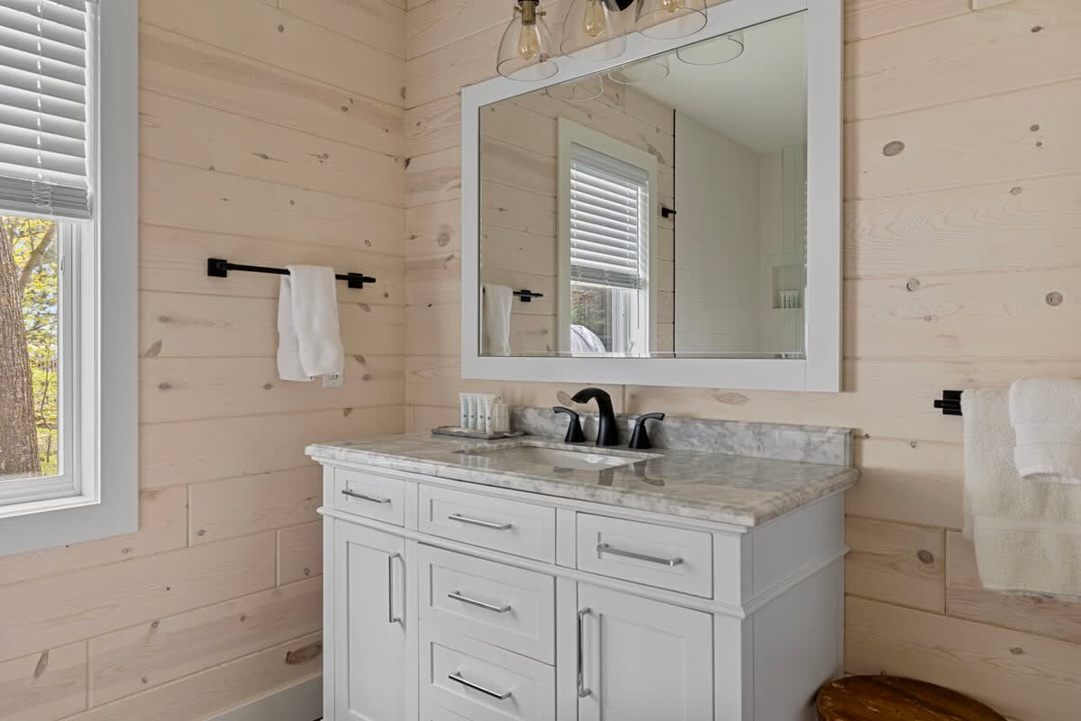 A beautifully accessorized bathroom with deluxe vanity + glass-wall shower-tub.
