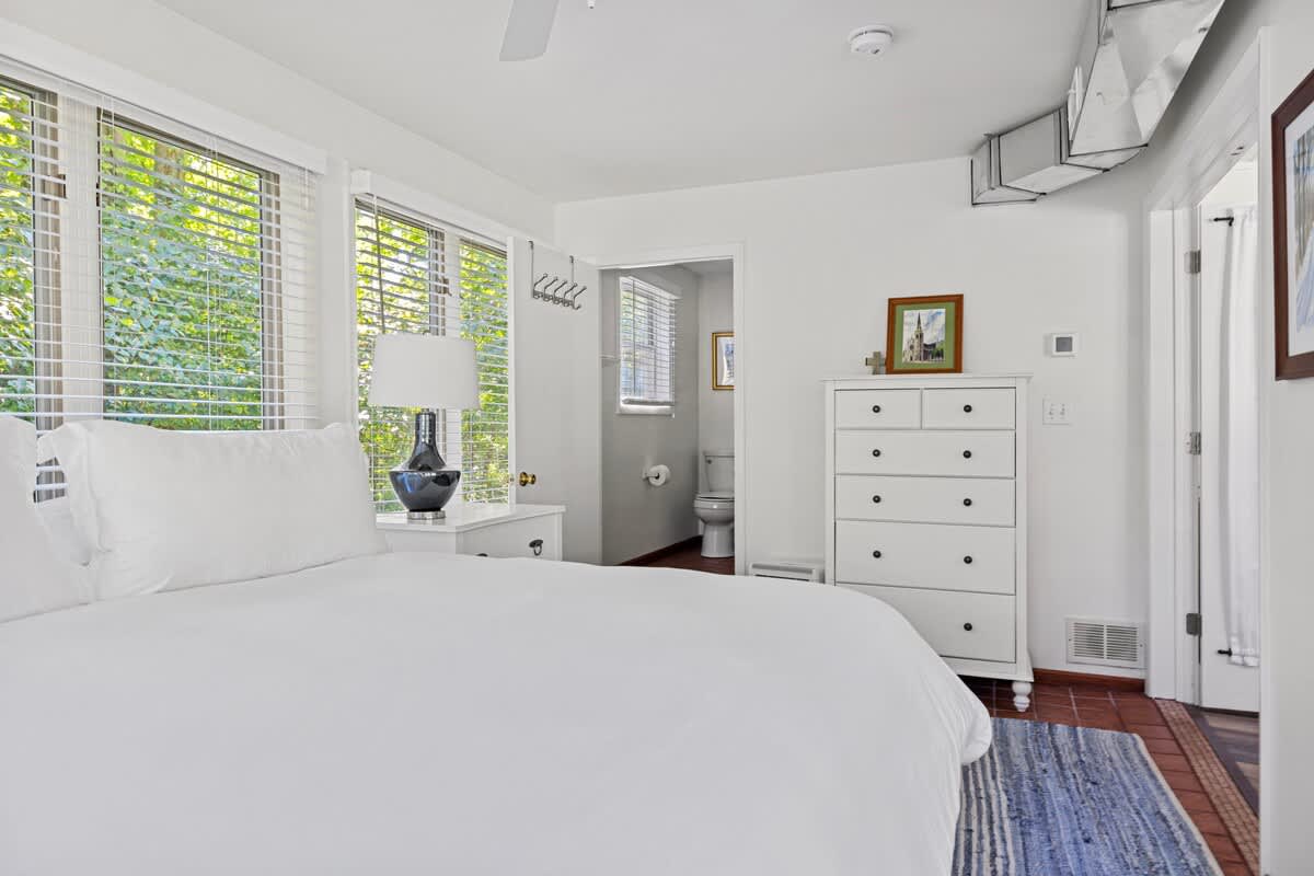 Clean lines and calming whites create a serene escape in this bedroom, complete with a spacious dresser and a cozy corner for relaxation.