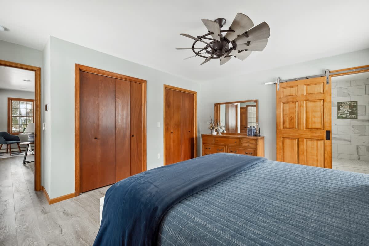 This inviting bedroom blends warm wood tones, soft blue hues, and a stunning farmhouse-style fan for the perfect retreat. Would you love to wake up here?
