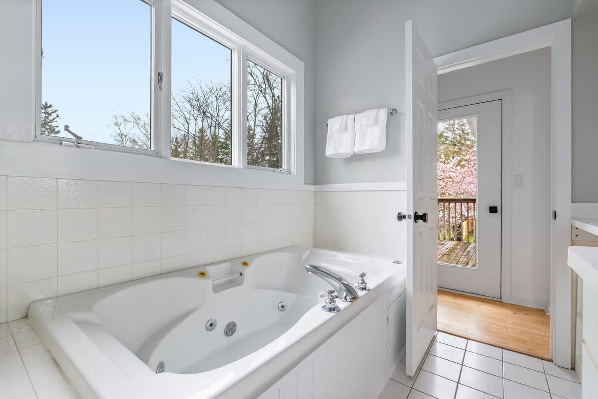 Spa day at home with a large jetted tub, serene natural light, and even a door that opens right out to the fresh air and cherry blossoms. The perfect spot to unwind in style.