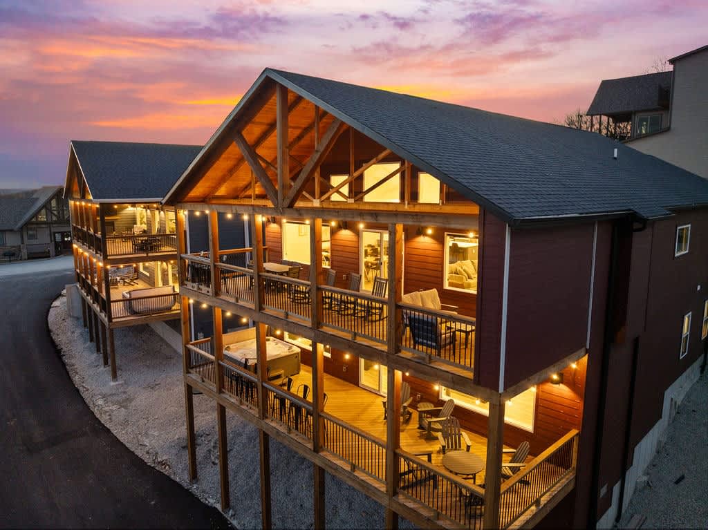 Twilight view of the large deck spaces with string lights, hot tub, drink rails, and plenty of seating for everyone!
