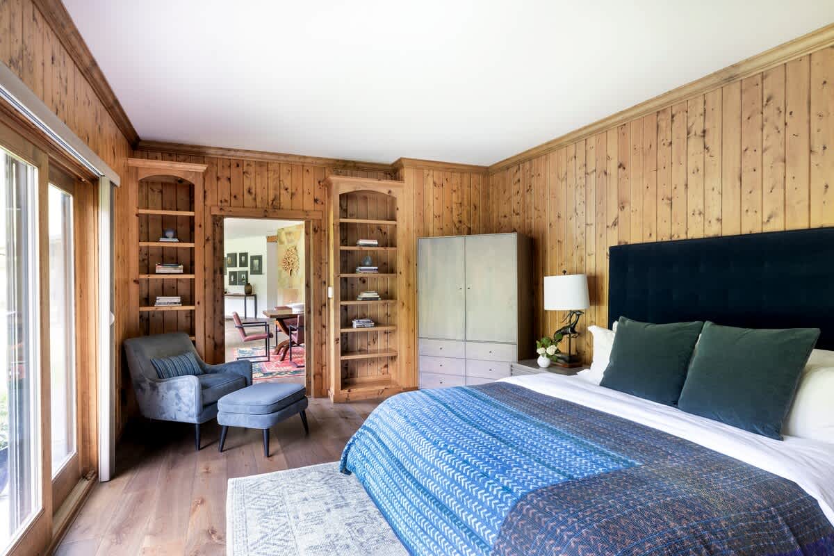 Bedroom #2 features warm wood paneling, access to a patio, and a peaceful view of rolling hills. 