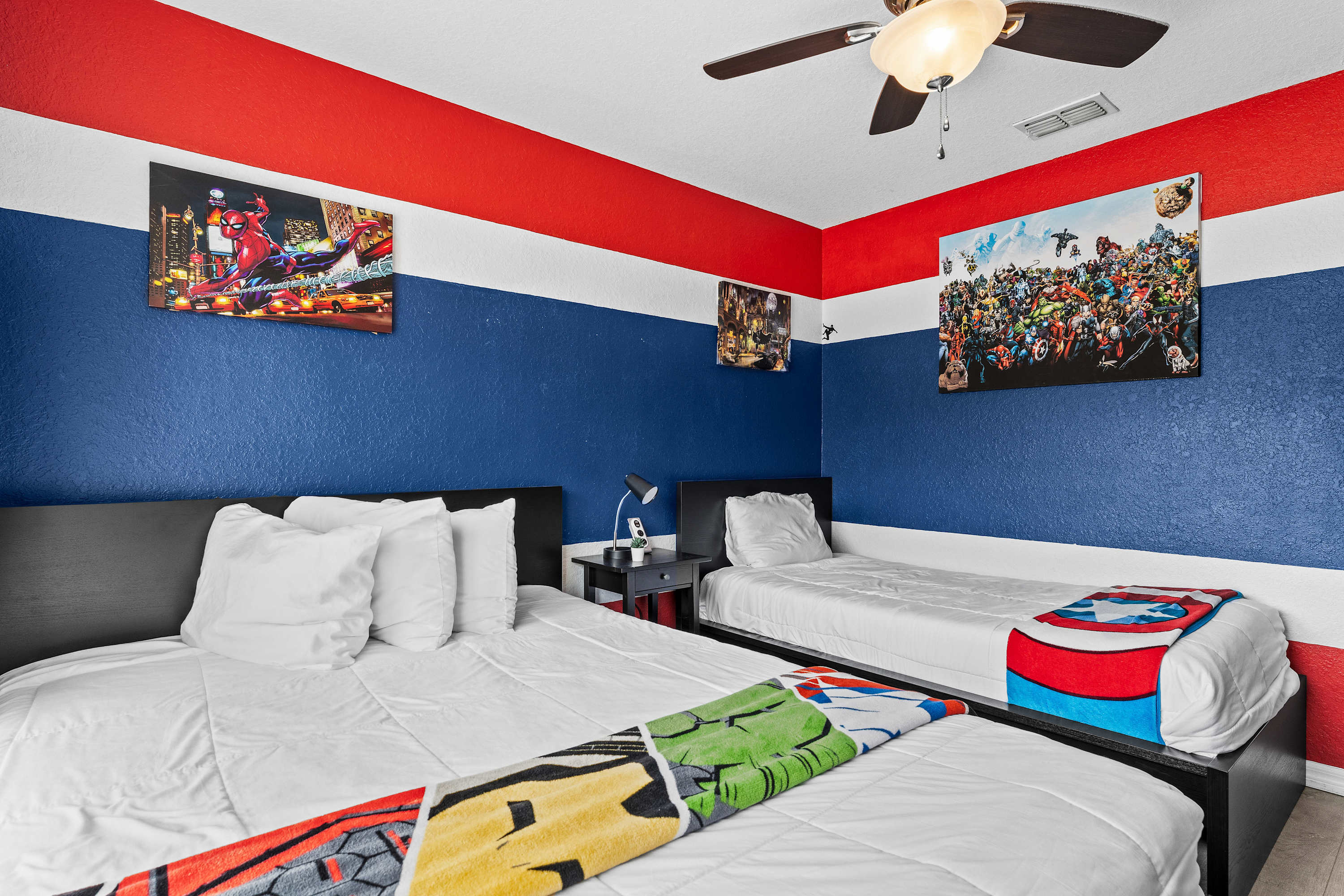 Marvel-themed bedroom with a twin and full bed, ceiling fan, and dedicated desk space