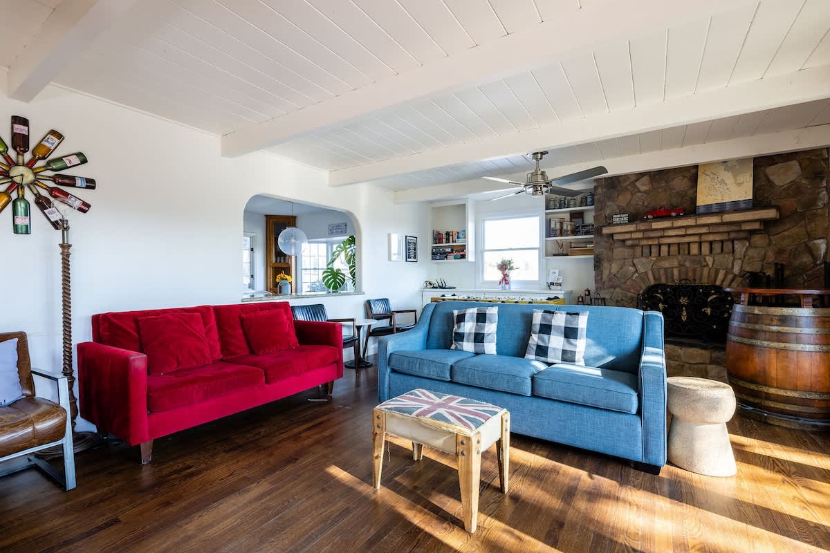 Spacious living room with bold modern sofas, a rustic stone fireplace, and open flow to the kitchen—perfect for families, wine lovers, golfers, and corporate retreats.