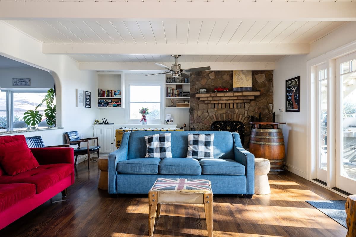 Cozy living room with a stone fireplace, colorful seating, and natural light—ideal for wine country getaways, family gatherings, or relaxing after golf and vineyard tours
