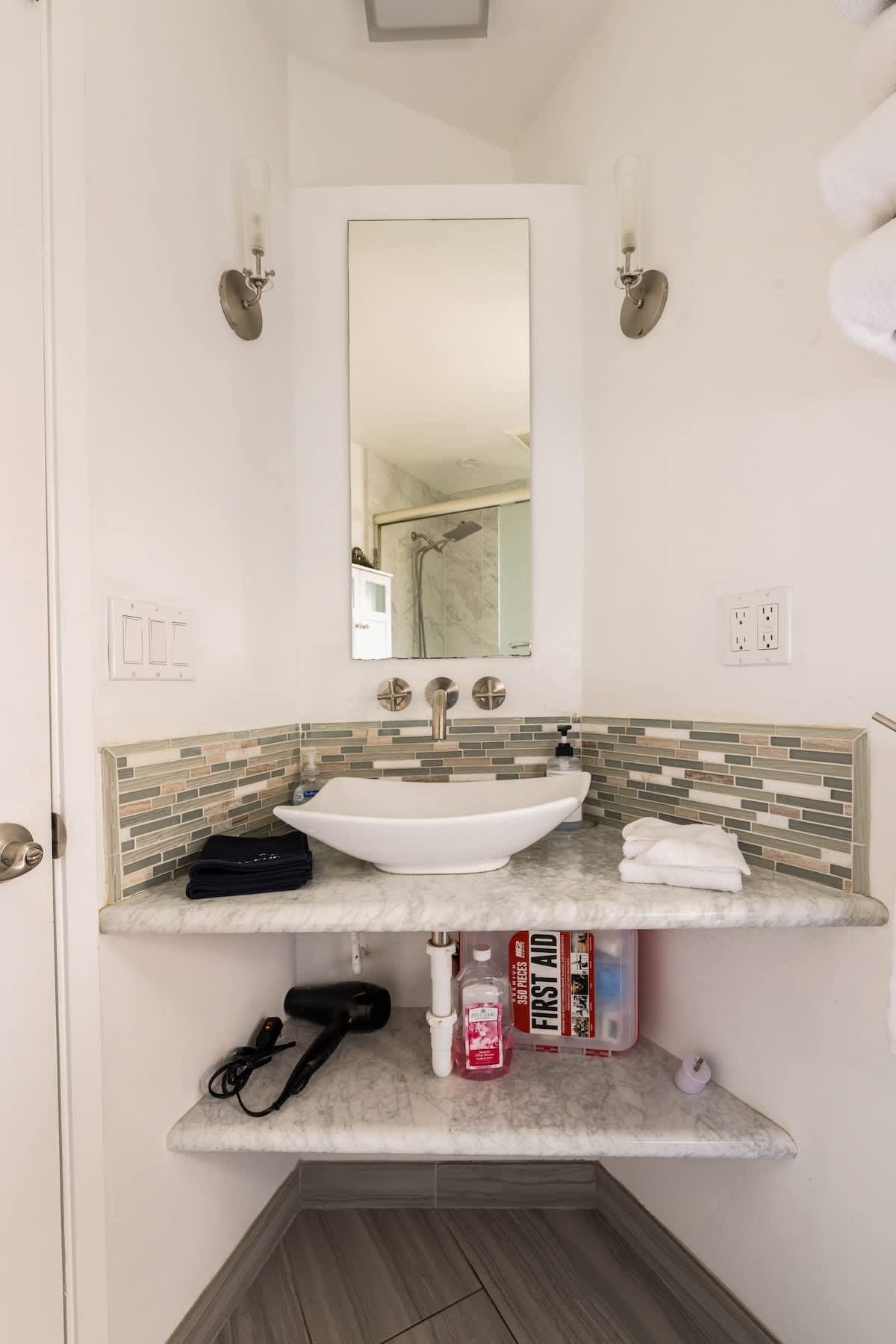 Modern vanity with a sleek vessel sink, marble counter, and mosaic backsplash. Essentials like a hair dryer, first-aid kit, and fresh towels are thoughtfully stocked for your comfort.