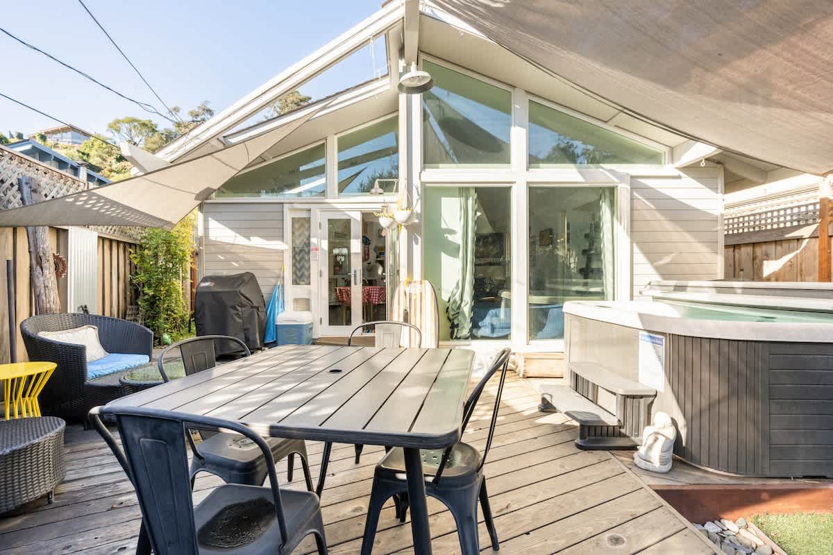 Bright patio with dining, lounge seating, and hot tub access — ideal for romantic evenings, family BBQs, or business travelers enjoying a coastal retreat.