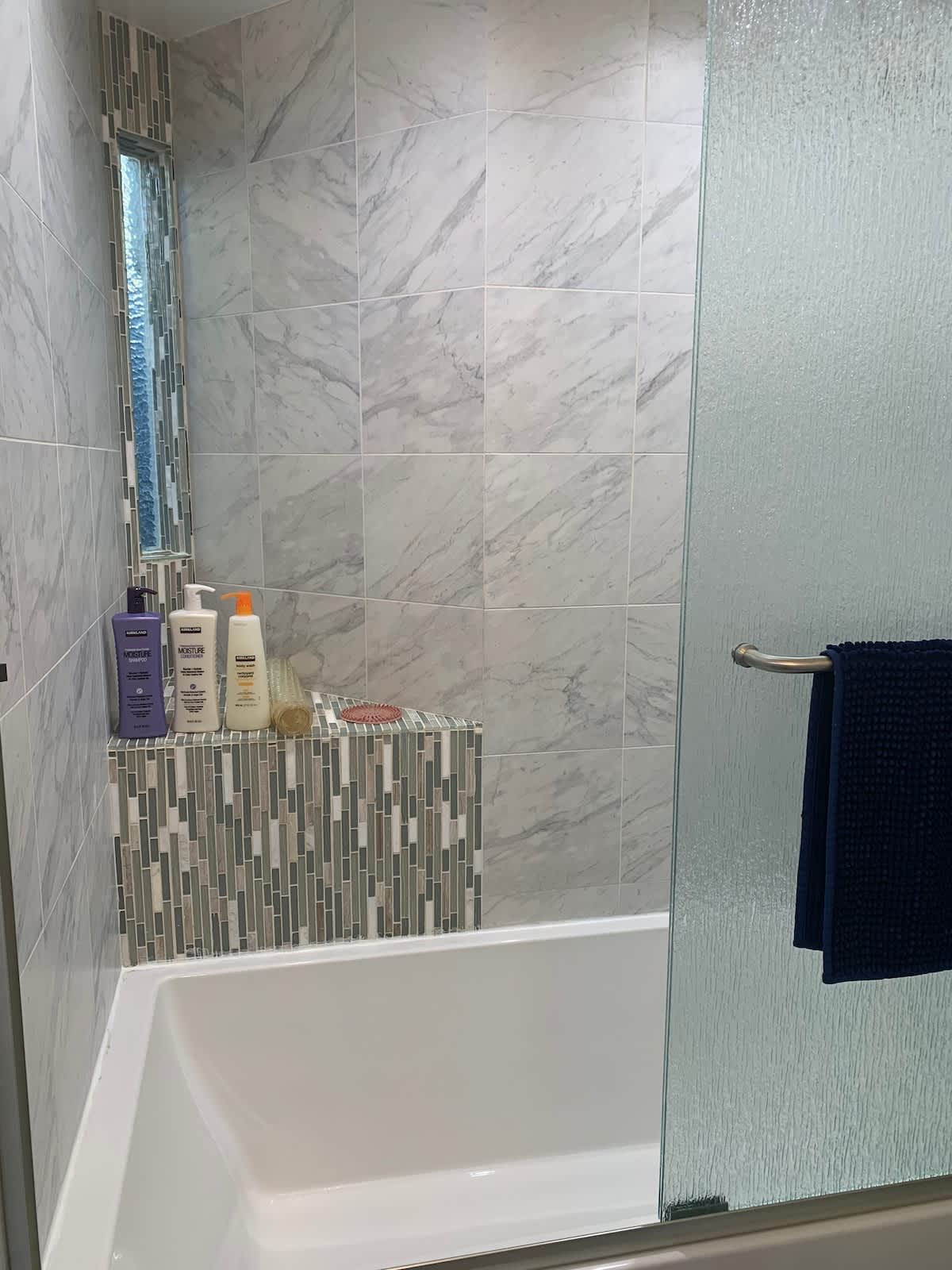 Bright full bathroom with marble tile, rainfall showerhead, and glass door enclosure—modern design and spa-like comfort for your stay.