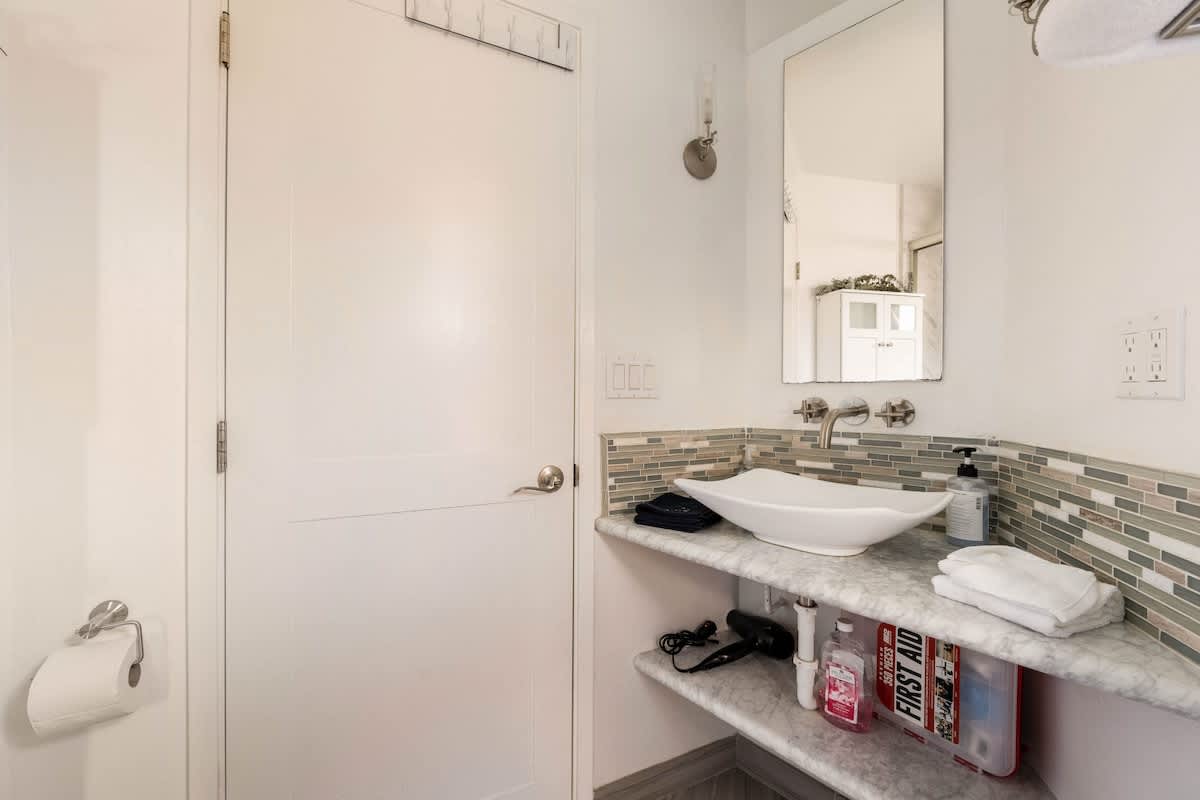 Bright full bathroom with marble counters, vessel sink, and stylish backsplash—modern design meets comfort.