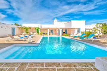 Swimming pool with sun loungers in front of a villa
