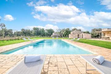 Limestone villa with grey shutters behind a pool