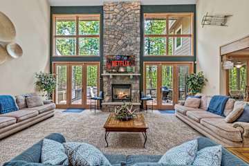 Spread out across three facing sofas, with the stone fireplace as the room’s anchor and deck doors on either side.
