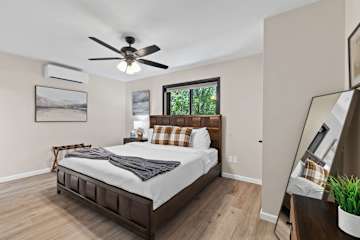Claim the primary suite and sleep like it's the best version of a hotel night — king bed with a solid wood panel frame, blackout shades, and a ceiling fan turning slow above you.