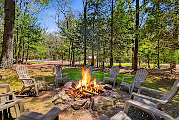Your stone fire pit circle is always ready — Adirondack chairs ringing the fire, tall pines overhead, and zero distractions from what actually matters.
