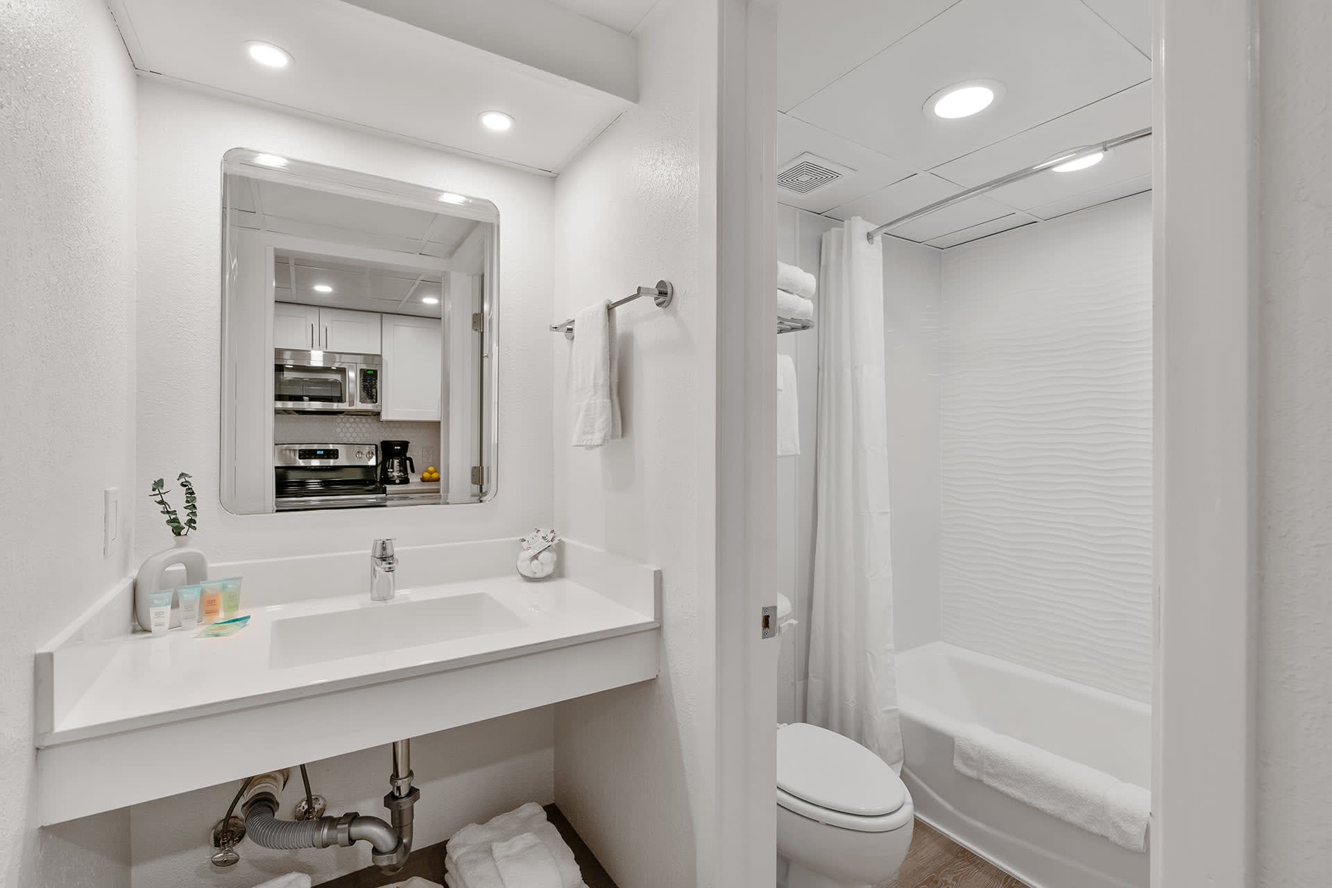 A bright, modern bathroom with crisp white tiles, a relaxing bathtub, and plush towels awaits your stay! 
