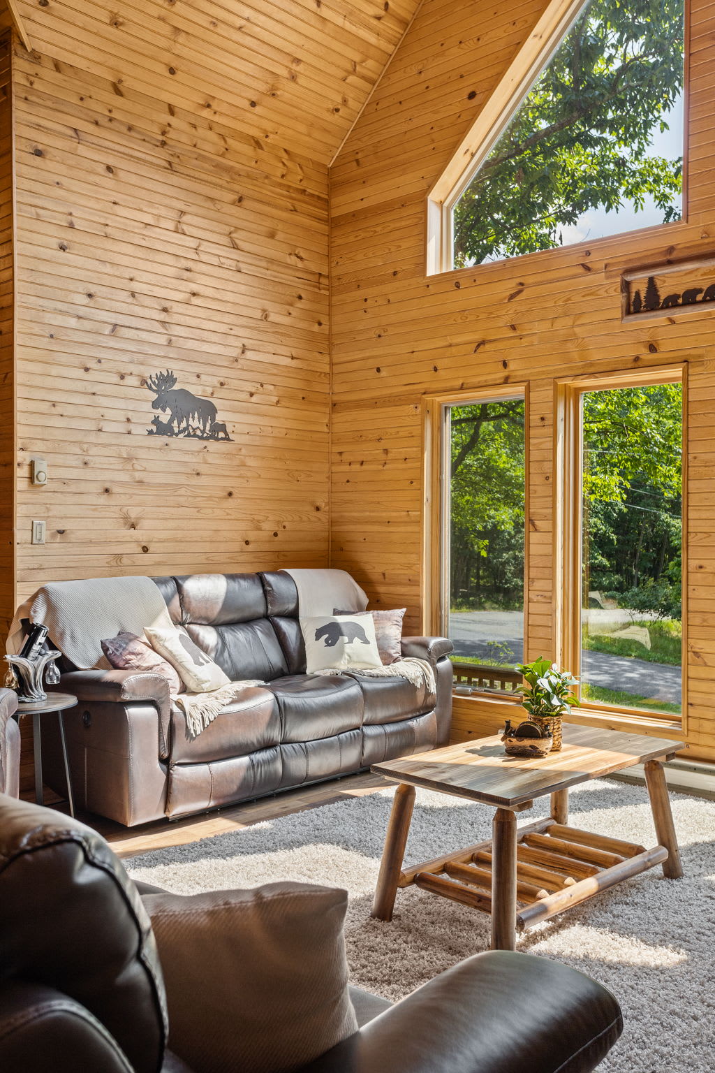 This cozy leather sofa, adorned with charming wildlife-themed accents, sits perfectly in front of stunning windows that frame the surrounding greenery.