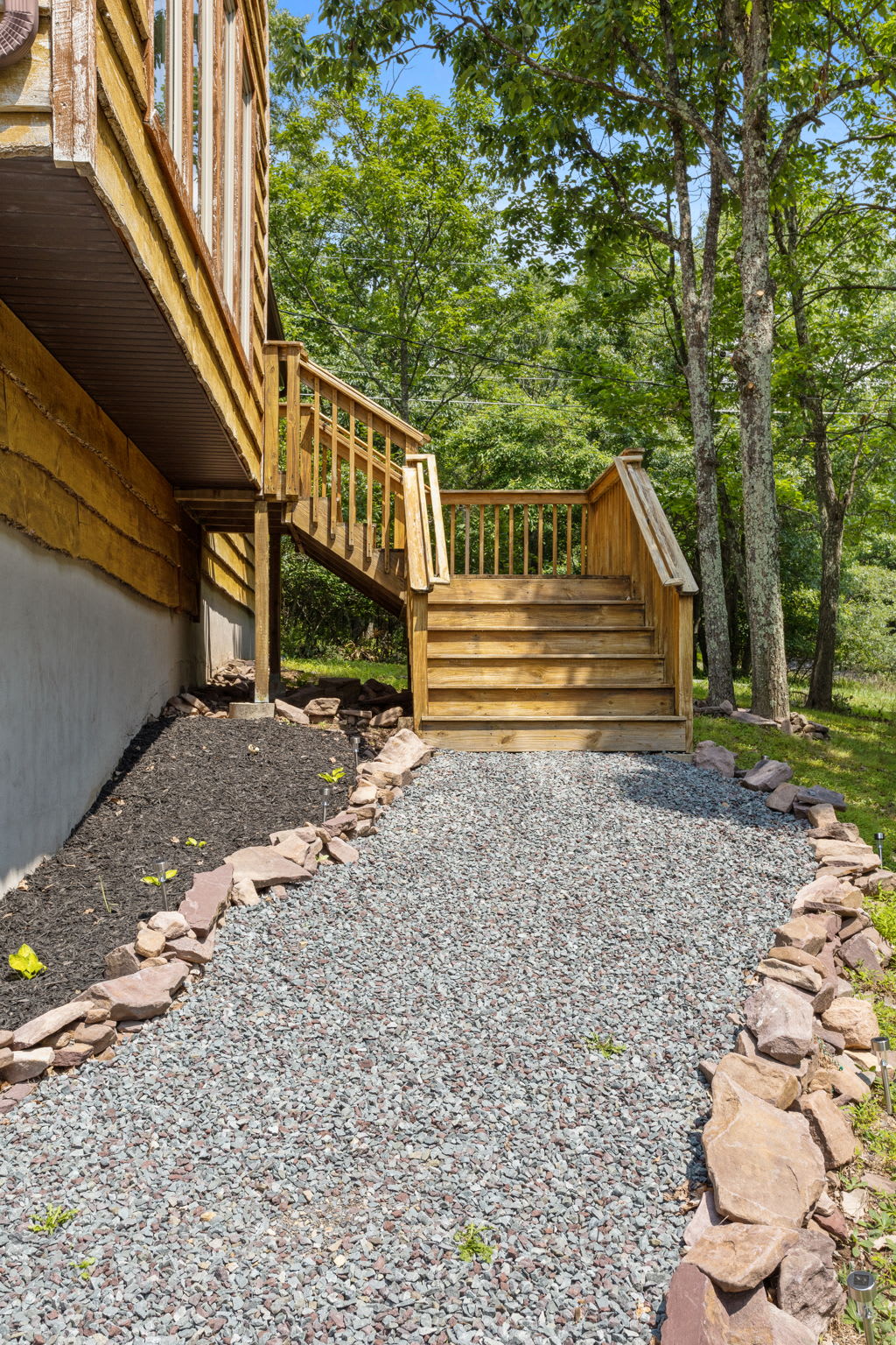 A beautifully crafted stone-lined walkway leads to the welcoming wooden stairs of this nature-inspired retreat.