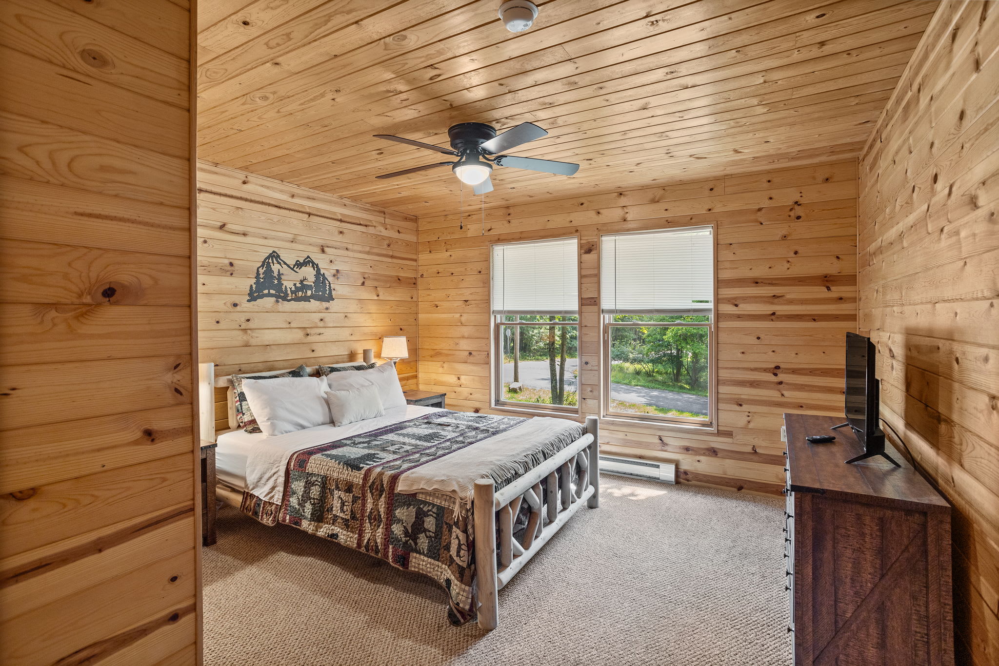 Unwind in this warm and inviting bedroom, complete with wood-paneled walls, a comfy bed, and large windows that bring in plenty of natural light.